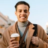 Young man smiling and drinking coffee while walking